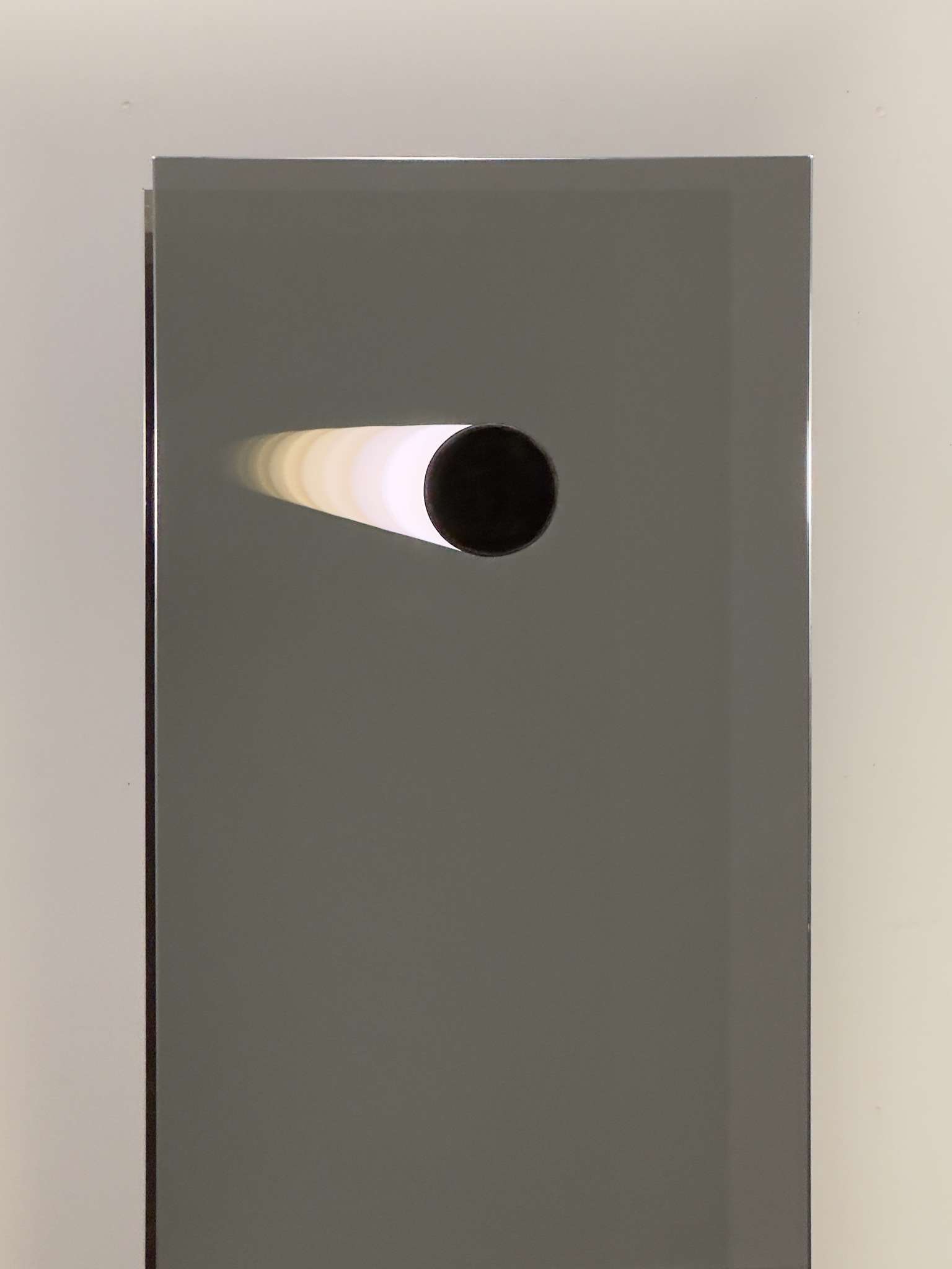 The tube's light reflects in mirrors, evoking an endless tunnel of light, blending space and time perception inseparably.