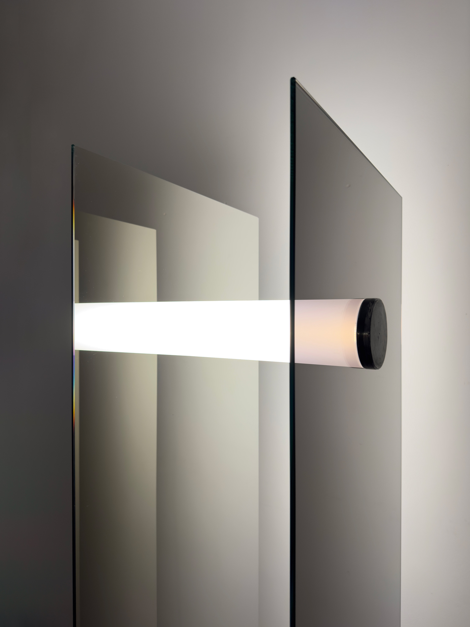Horizontal luminous tube held by two vertical and parallel one-way mirror plates, creating a depth effect from a steel cap.