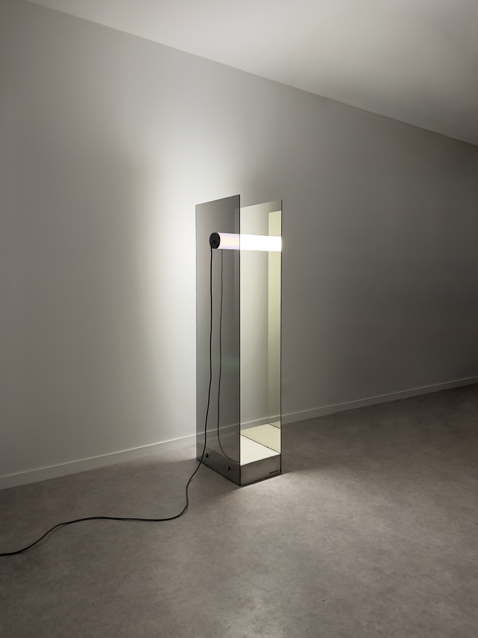 Minimalist floor sculpture 'Equation Keyboard' composed of a raw concrete block, a luminous tube, and two parallel one-way mirrors.