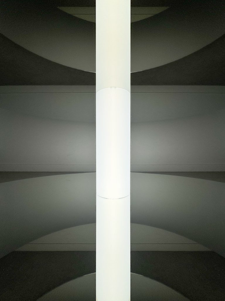 Central luminous tube of the sculptural artwork "Graduate Flatfoot" infinitely reflected by two parallel mirrors.