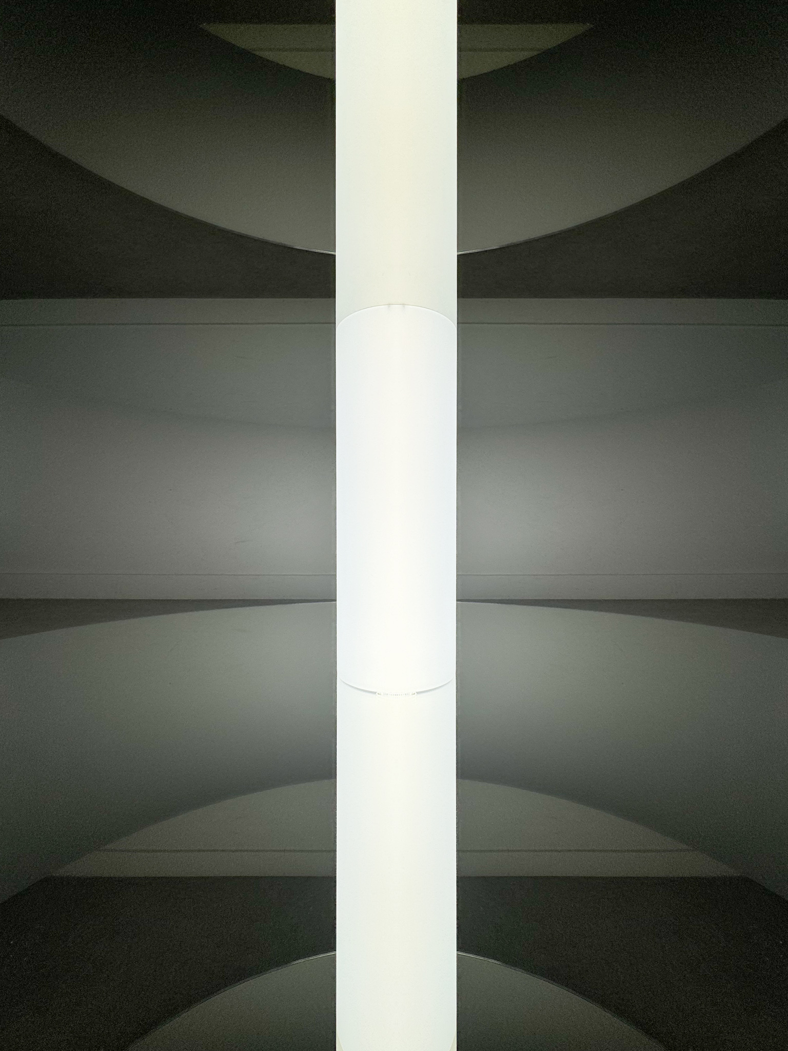 Central luminous tube of the sculptural artwork "Graduate Flatfoot" infinitely reflected by two parallel mirrors.