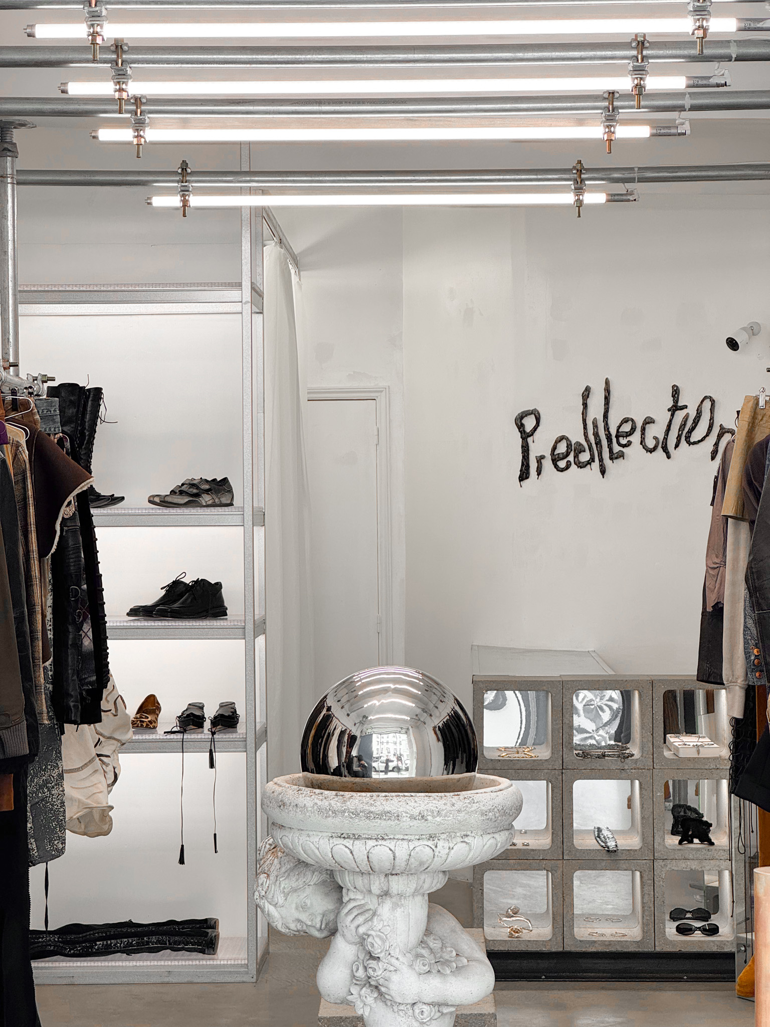 Predilection boutique interior with industrial decor, a stone statue with a silver sphere, mirrored display case, and bold wall art.