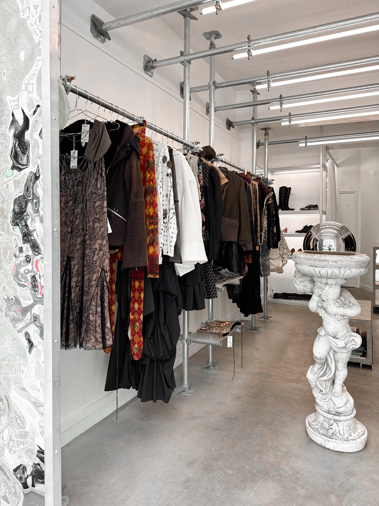 Minimalist fashion boutique "Predilection" with clothing on a metal rack, industrial décor, and a classical statue adding a vintage touch.