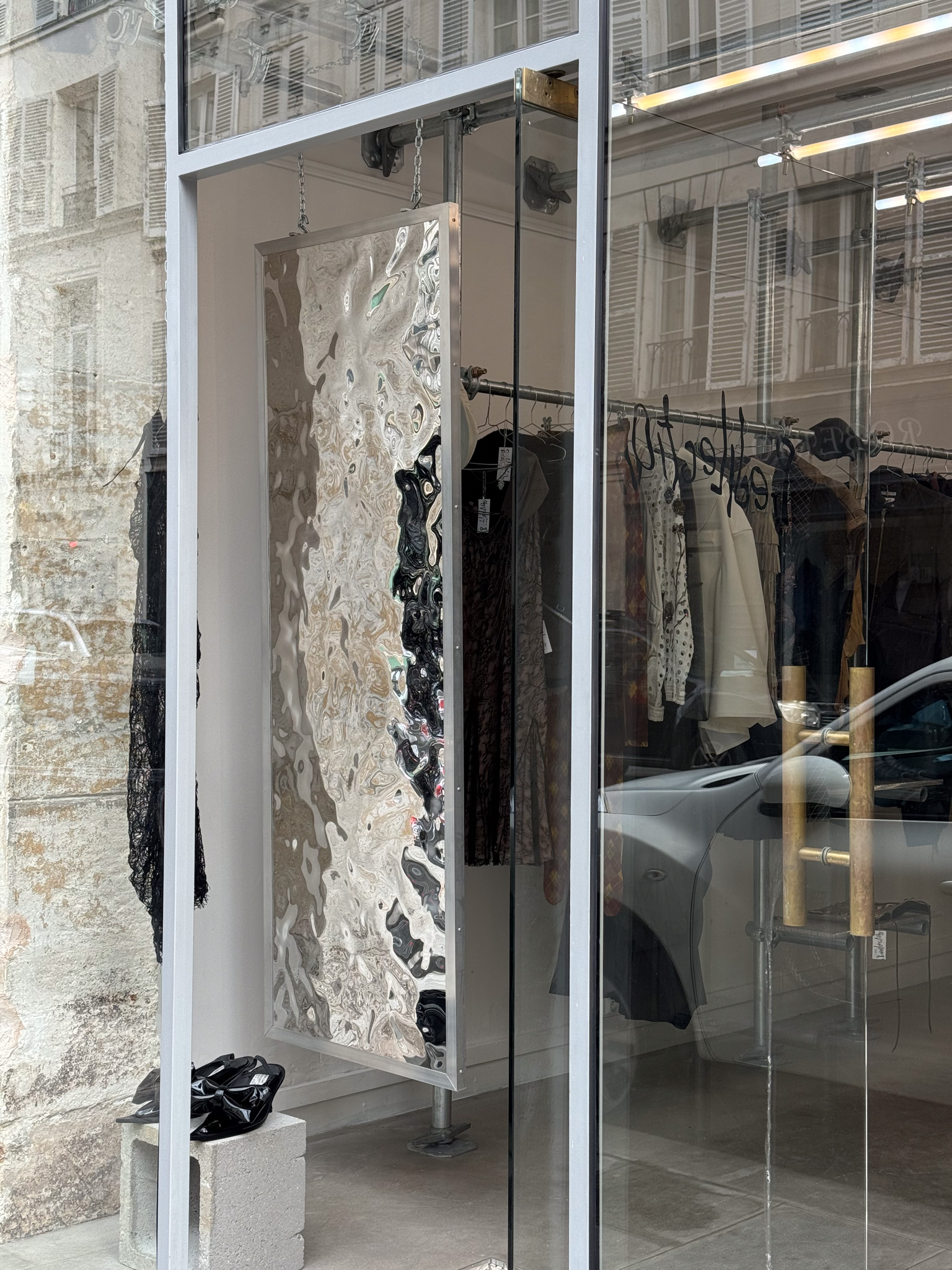 Close-up of Prédilection's storefront with Fabien Ficher’s artwork "Dismorphia," a wavy mirror, reflecting the raw industrial interior.