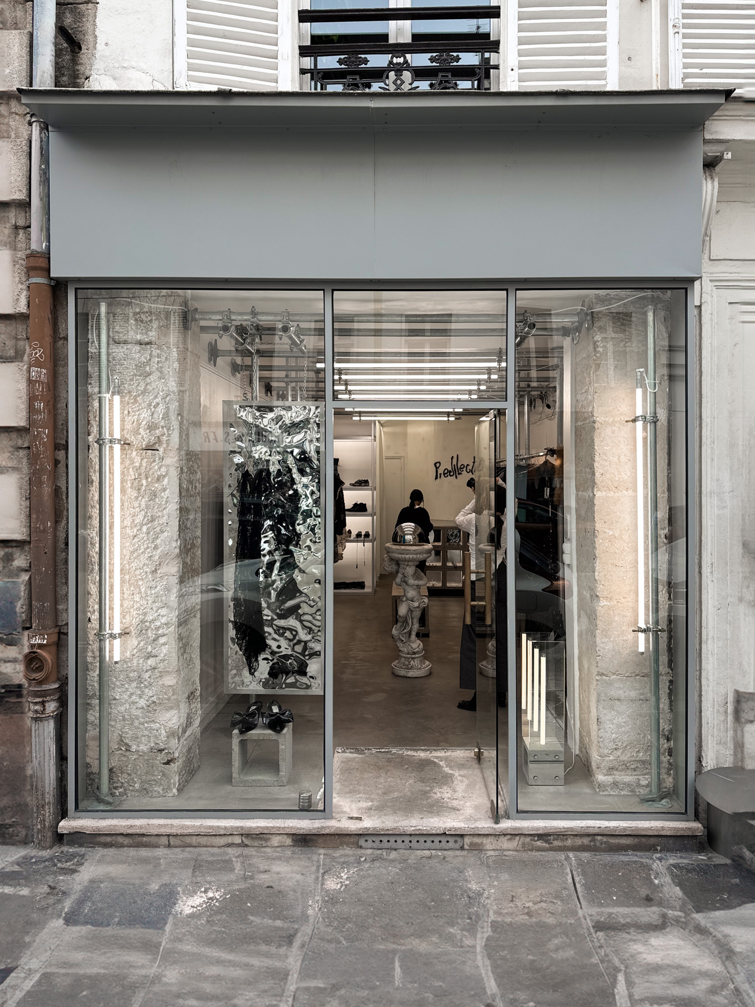 The Predilection storefront reveals an industrial interior with a central statue, scaffolding displays, and a modern, minimalist aesthetic.