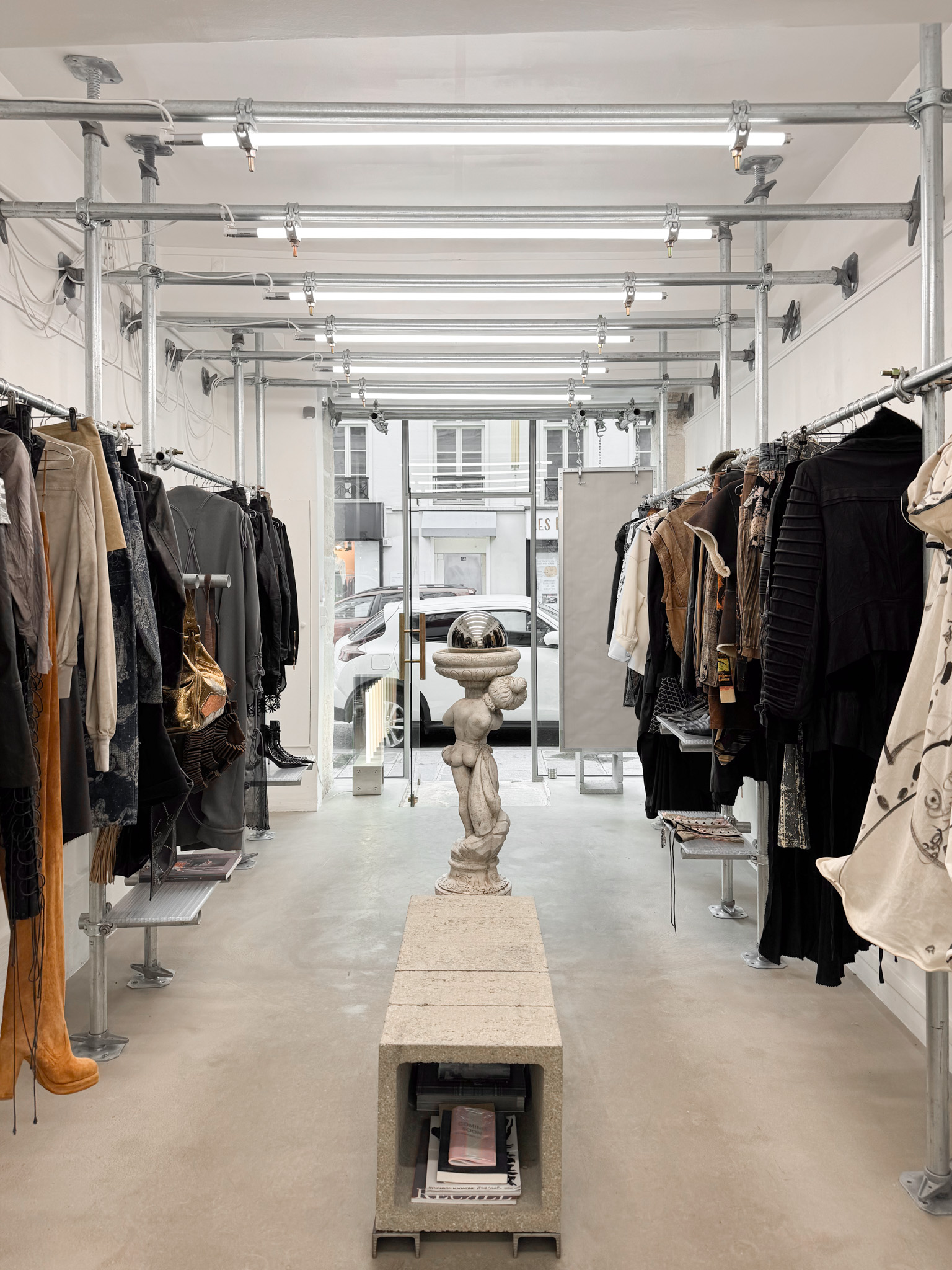 Predilection boutique’s industrial interior: galvanized steel racks, central statue, concrete bench, blending art, minimalism, and functionality.