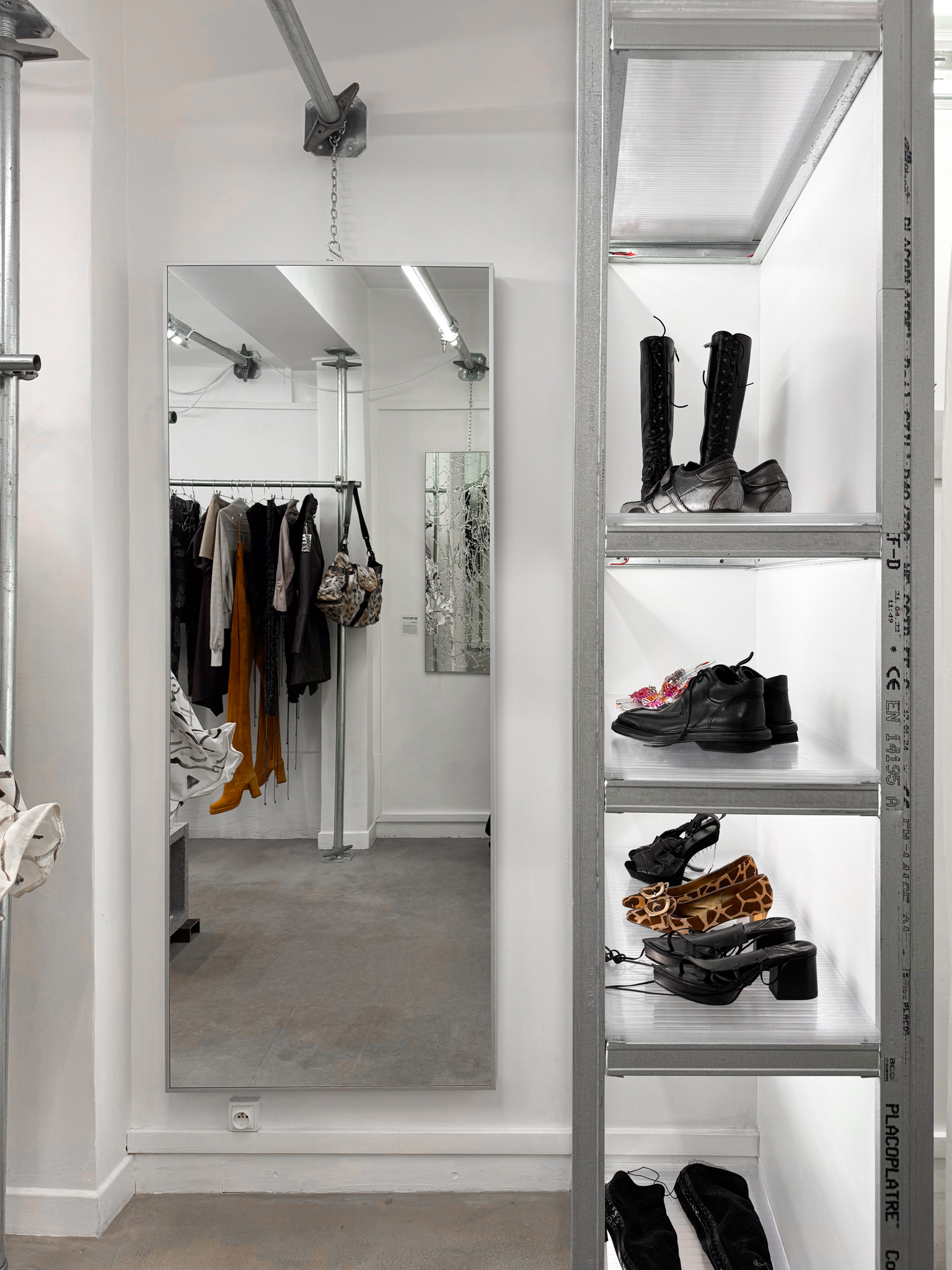 A modern boutique with galvanized steel shelving, a large mirror, and a minimalist industrial aesthetic. Neutral tones and raw materials dominate.