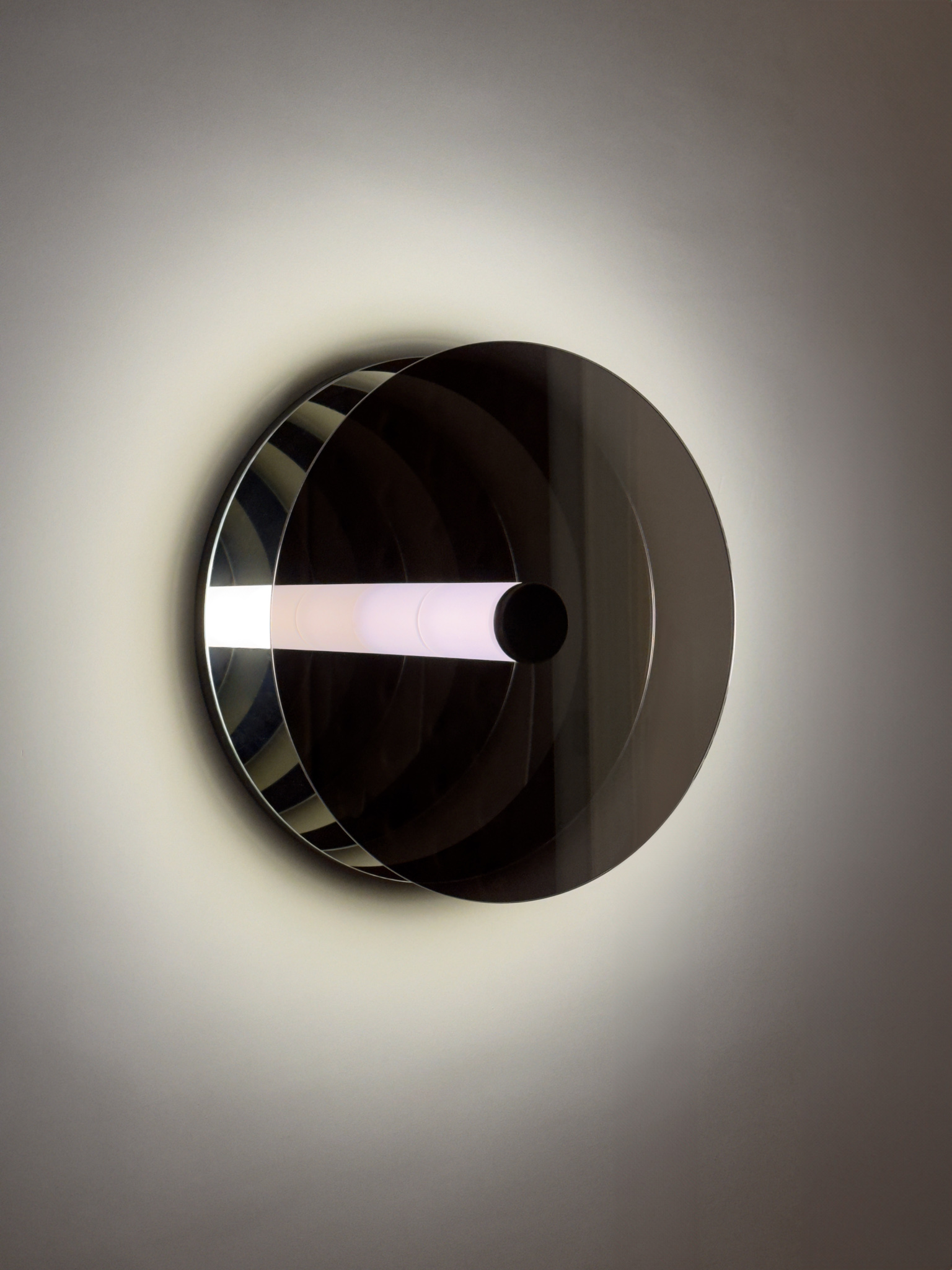 Paramount Ragtime is a circular wall sculpture with a glowing central tube and mirrored surfaces, creating infinite reflections and a dynamic play of light and space.